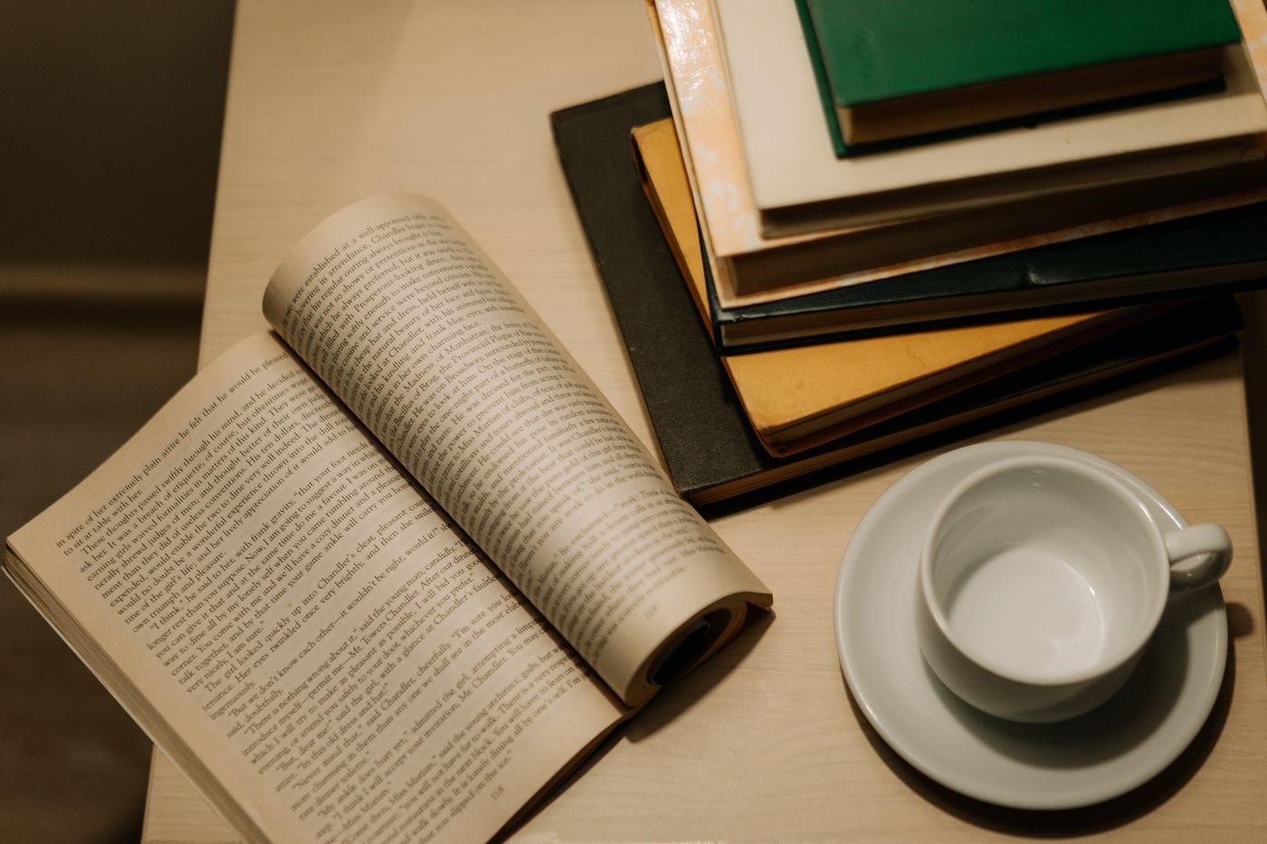 Открытая книга, чашка и стопка книг на деревянном столе